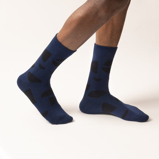 Model walking in navy crew socks with a black abstract half-circle pattern, shown mid-step against a white background.