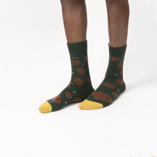 A model wearing dark green socks with a brown cookie print and yellow toes, shown against a plain white studio background.