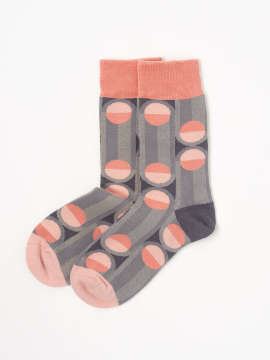 A pair of crew socks with a gray and pink striped pattern, featuring circular dot motifs and solid pink cuffs, heels, and toes, displayed on a clean white background.