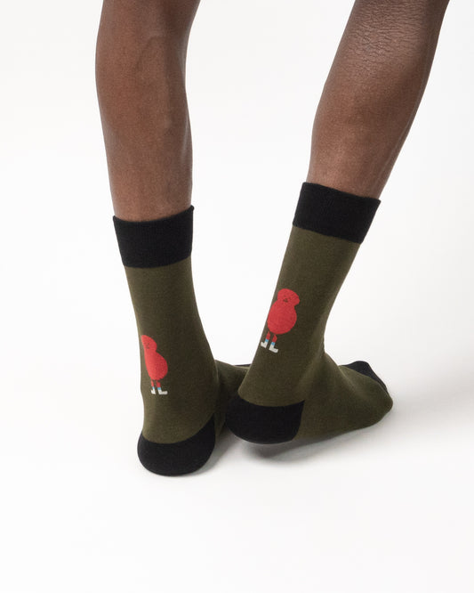 Olive green crew socks with black cuffs, heels, and toes, featuring a small red bird graphic on the side, shown on a model's feet against a white background.