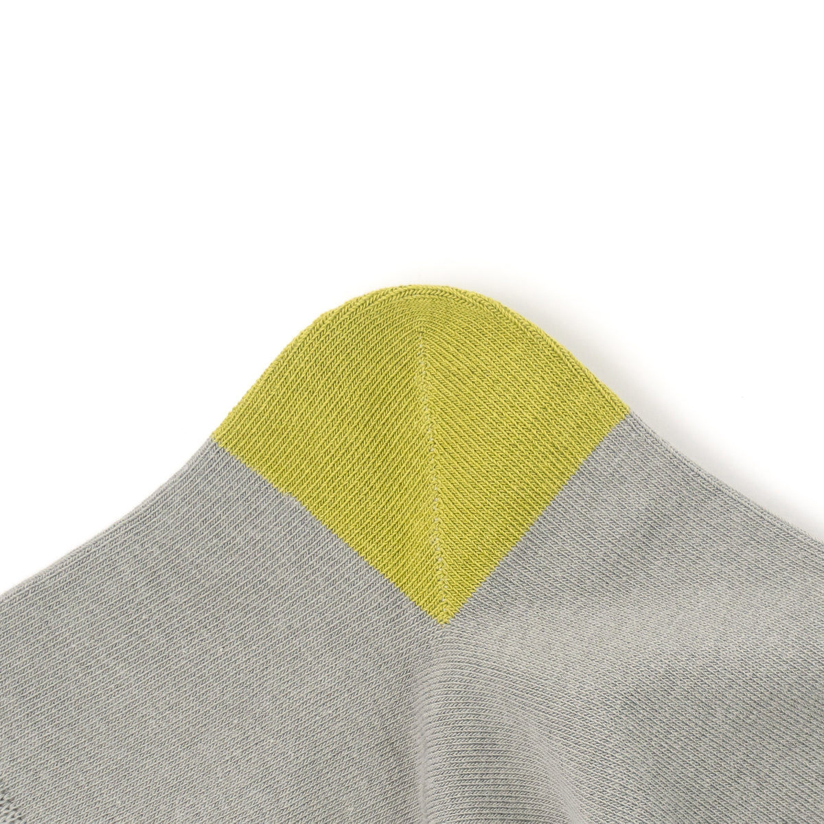 Close-up of a knit product corner showing a light gray ribbed fabric with a contrasting light yellow-green triangular section on a white background.