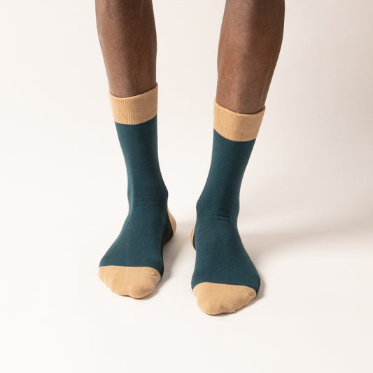 Model standing in deep teal crew socks with tan cuffs and toes, viewed from the front against a white background.