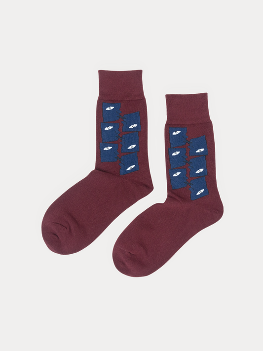 A pair of crew socks in a deep burgundy color, featuring a vertical blue panel on the upper leg with a repeating pattern of small white fish, displayed against a light gray background.
