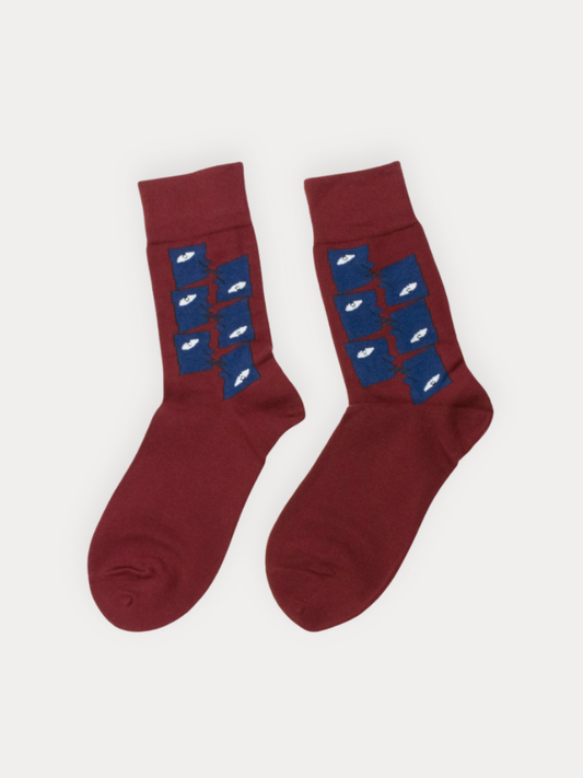 A pair of burgundy crew socks with a blue geometric tile pattern featuring abstract white one-eyed face motifs down the leg.