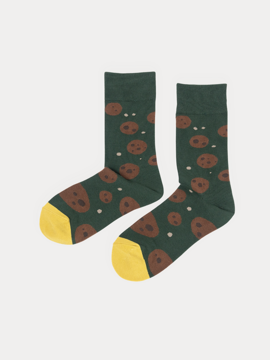 Pair of green crew socks with a chocolate chip cookie print and yellow toes, laid flat side by side.