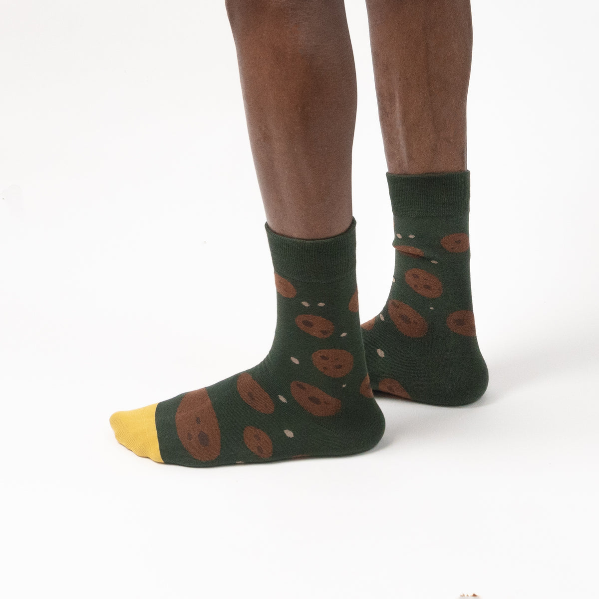 A person's feet wearing dark green crew socks with a brown cookie print and yellow toes, shown against a plain white background.