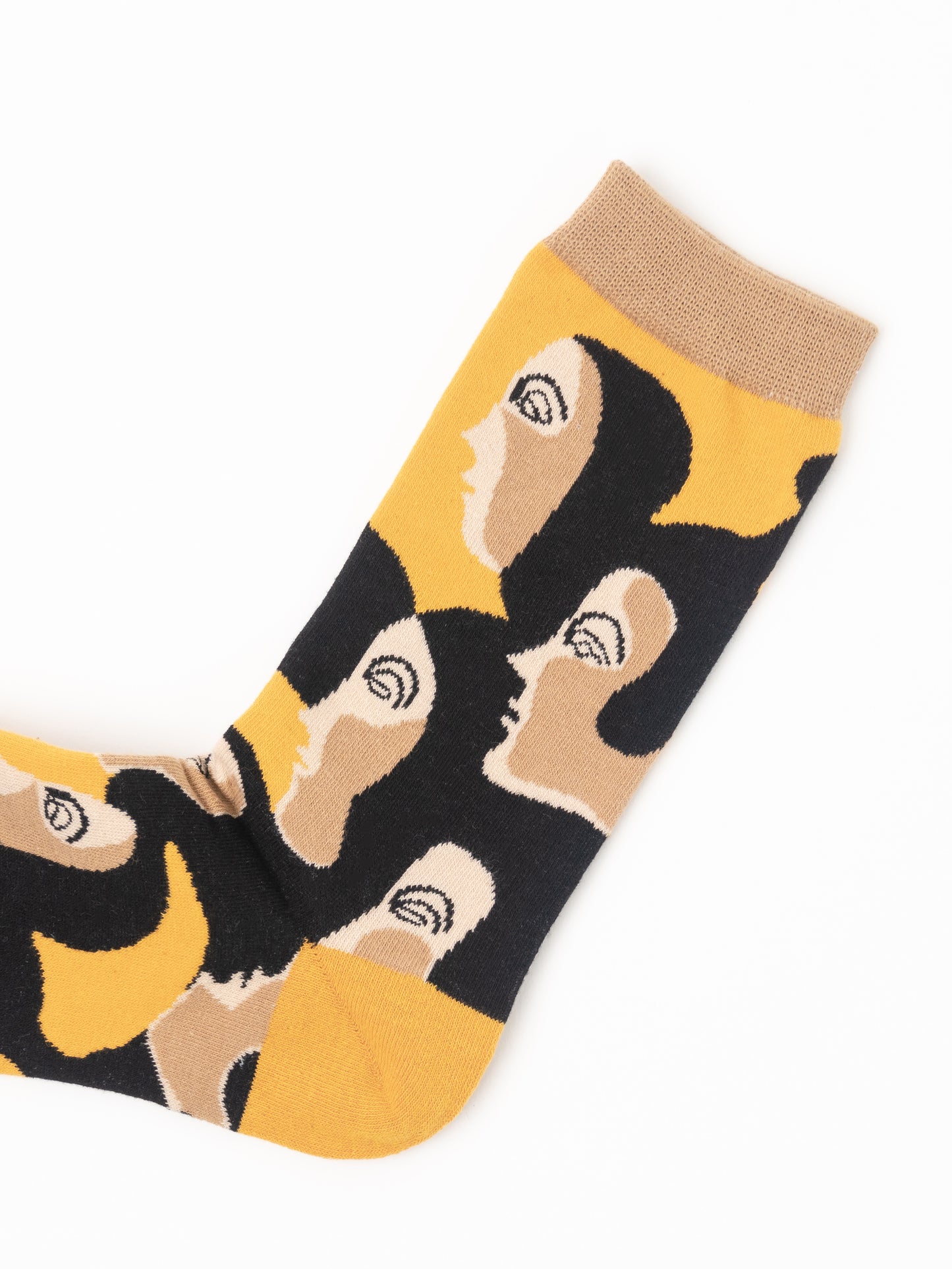 A single crew sock with a bold graphic pattern of stylized faces in black, beige, and mustard yellow, featuring a solid beige ribbed cuff, shown on a plain white background.