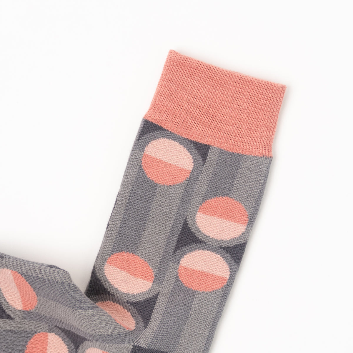 A close-up of a gray patterned sock with vertical stripes and large pink and white geometric circles, featuring a solid pink ribbed cuff, shown on a white background.