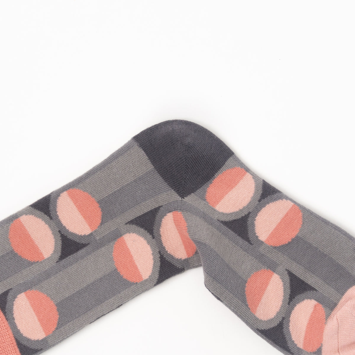 A close-up of a gray patterned sock with alternating pink and peach circular motifs, laid flat on a white background.