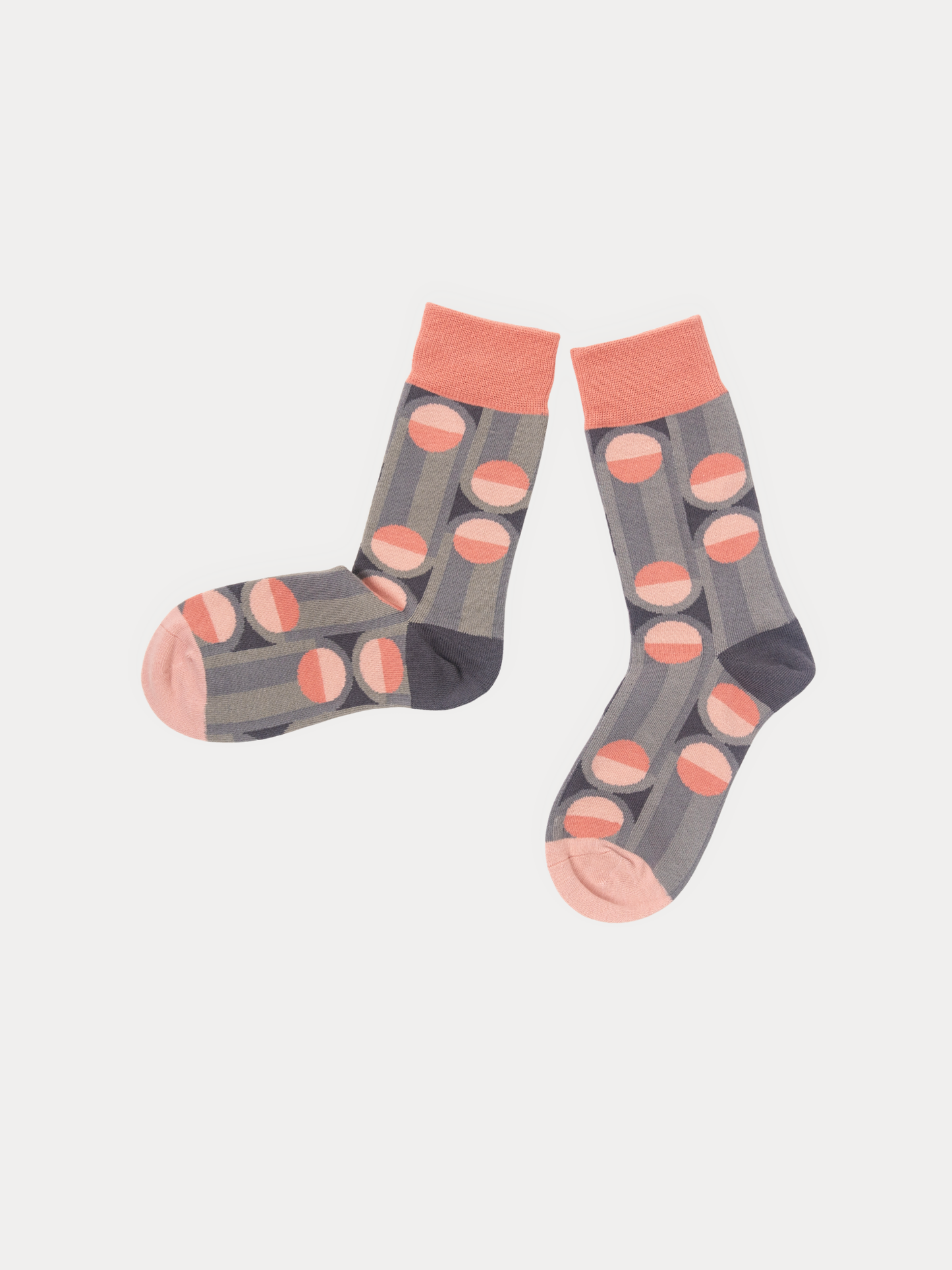 A pair of crew socks with a gray and dark gray striped pattern, decorated with pink and peach polka dots, featuring solid peach cuffs and toes, displayed on a light gray background.