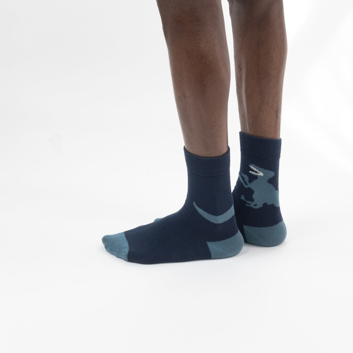 A model wears navy blue crew socks with a light blue-gray dinosaur graphic on the sides, shown against a plain white background.