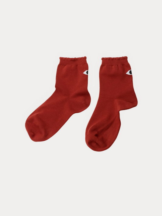 Pair of brick red ankle socks with a small black and white eye graphic on the cuff, laid flat.