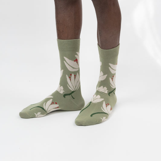 Three-quarter side view of a model wearing sage green crew socks patterned with large white flowers, green stems, and red center accents on a white background.