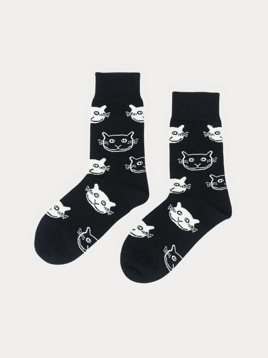 A pair of black crew socks with a white cartoon cat face pattern, displayed against a light gray background.