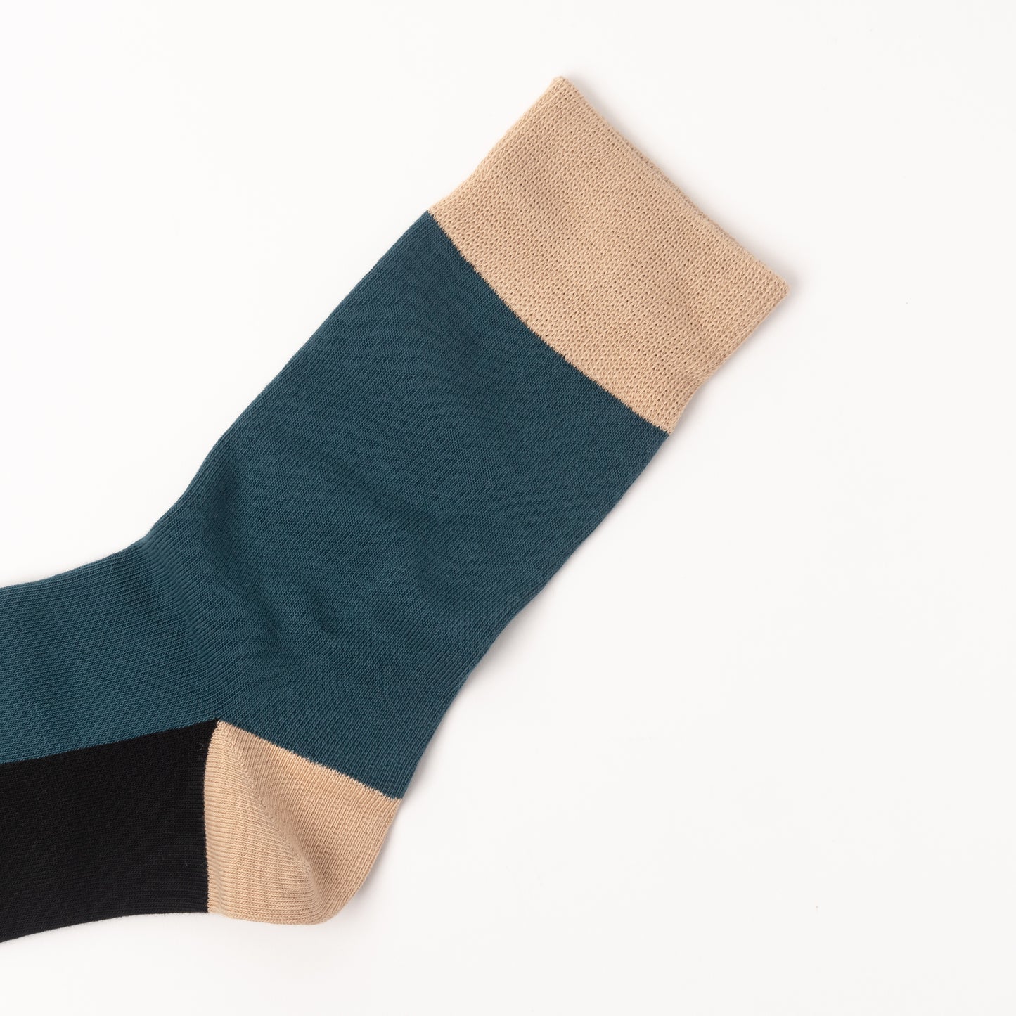 A single color-blocked sock laid flat on a white background, featuring a dark teal body, a beige cuff and toe, and a black heel section.
