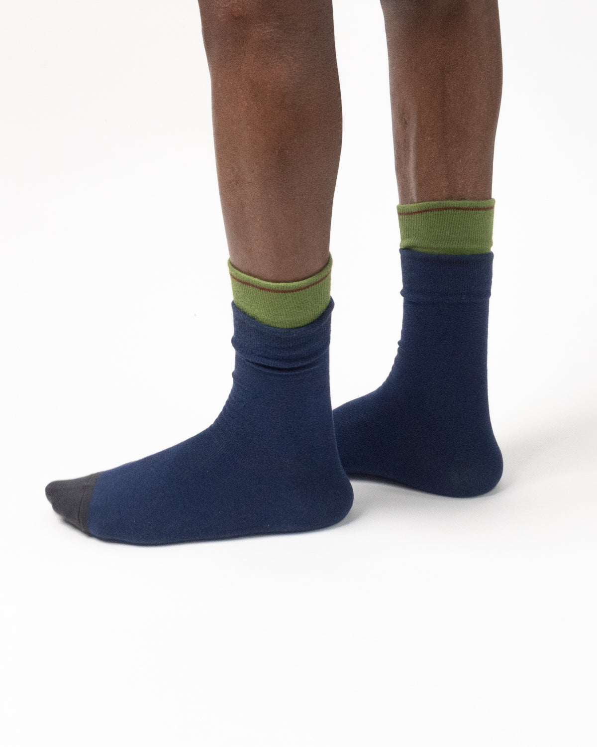 A pair of navy blue crew socks with olive green cuffs and dark gray toes, shown on a model's feet against a white background.