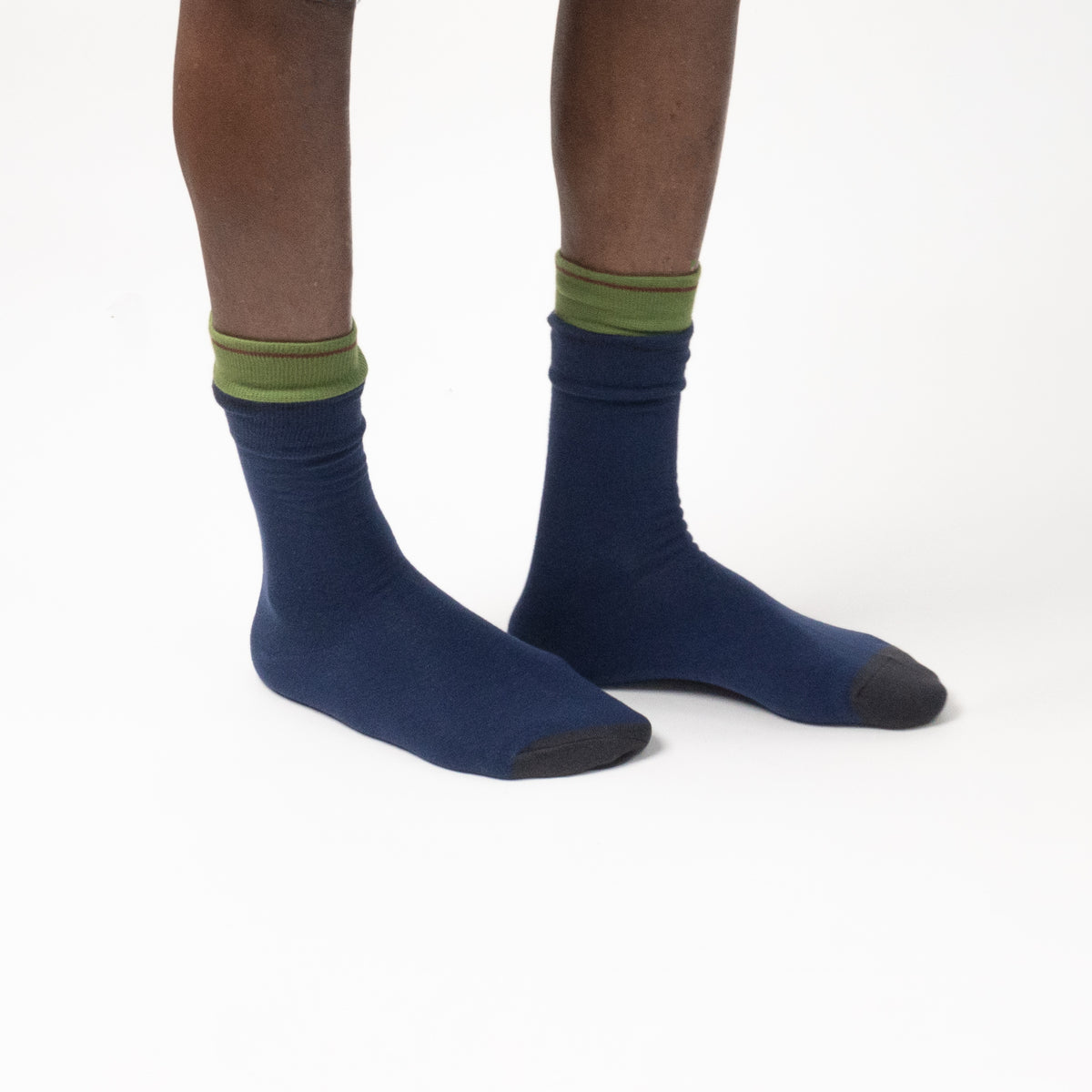 A person's legs wearing navy blue crew socks with olive green ribbed cuffs and dark gray toes, shown against a plain white studio background.