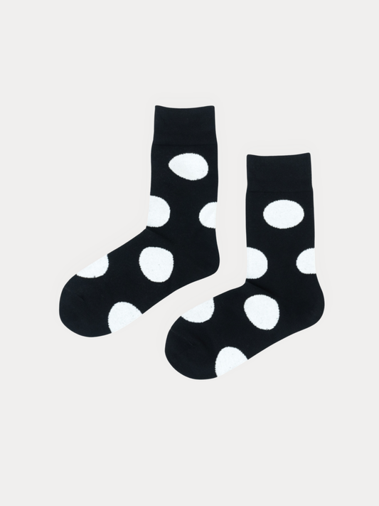 A pair of black crew socks with large white polka dots, displayed against a light gray background.