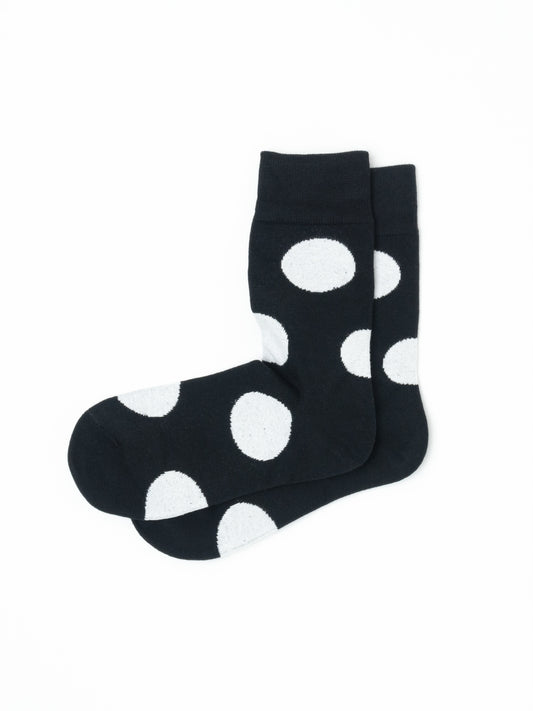 Pair of black crew socks with a bold white polka dot print, laid flat and overlapping at the ankle.
