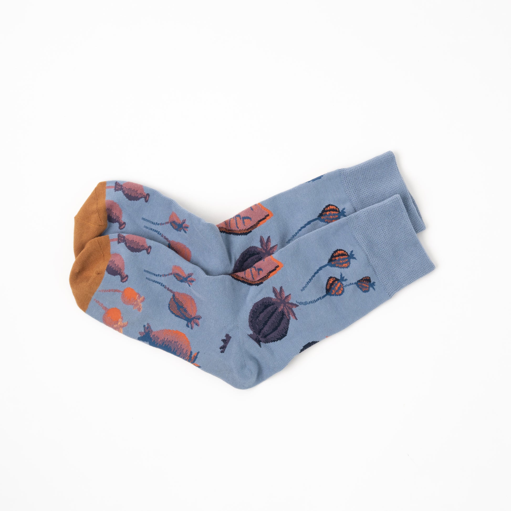 A pair of light blue crew socks with a botanical pattern of orange and dark purple poppy pods, featuring solid orange toes, is displayed on a clean white background.