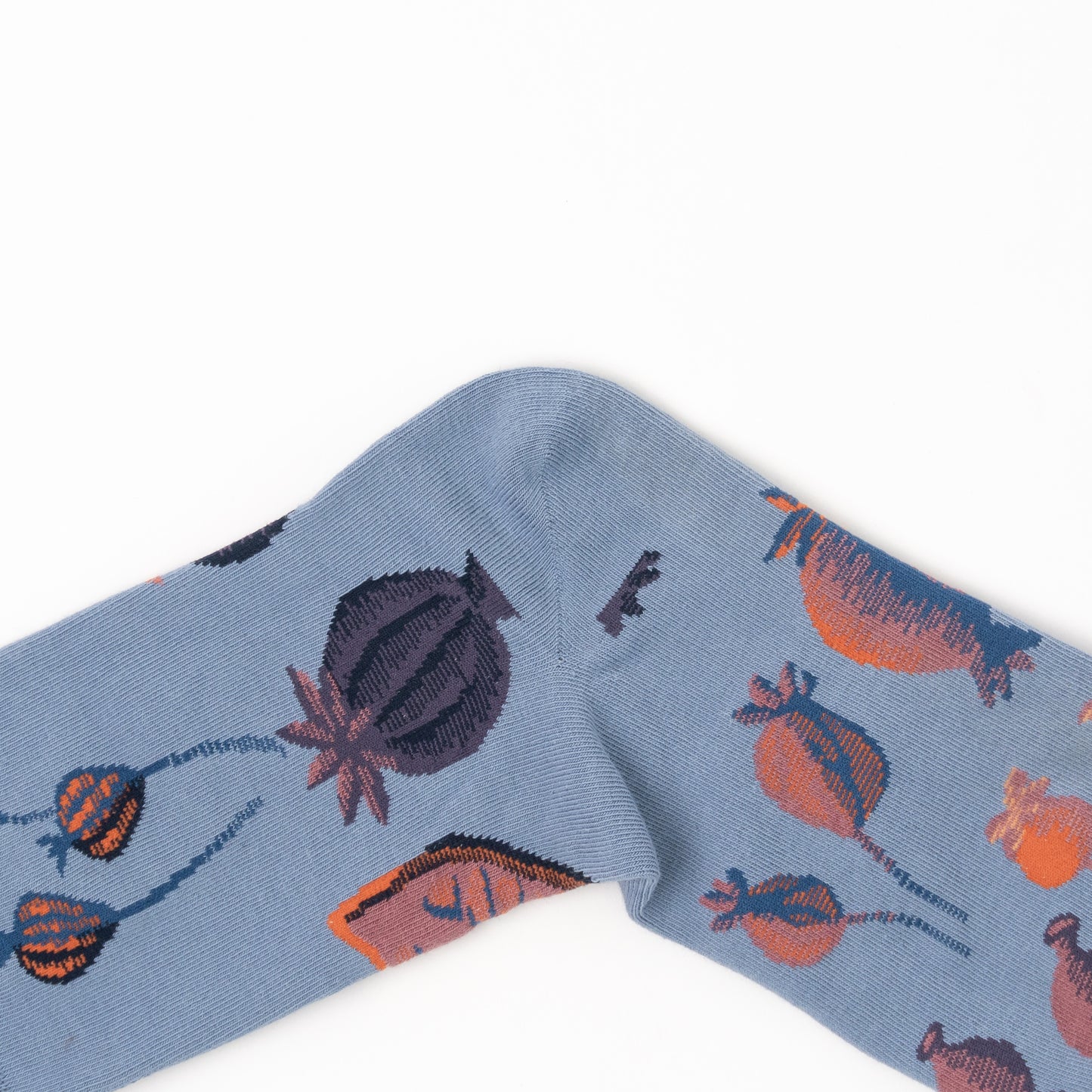 Close-up of a folded sock's heel, showing large orange and plum poppy pod illustrations on dusty blue fabric.