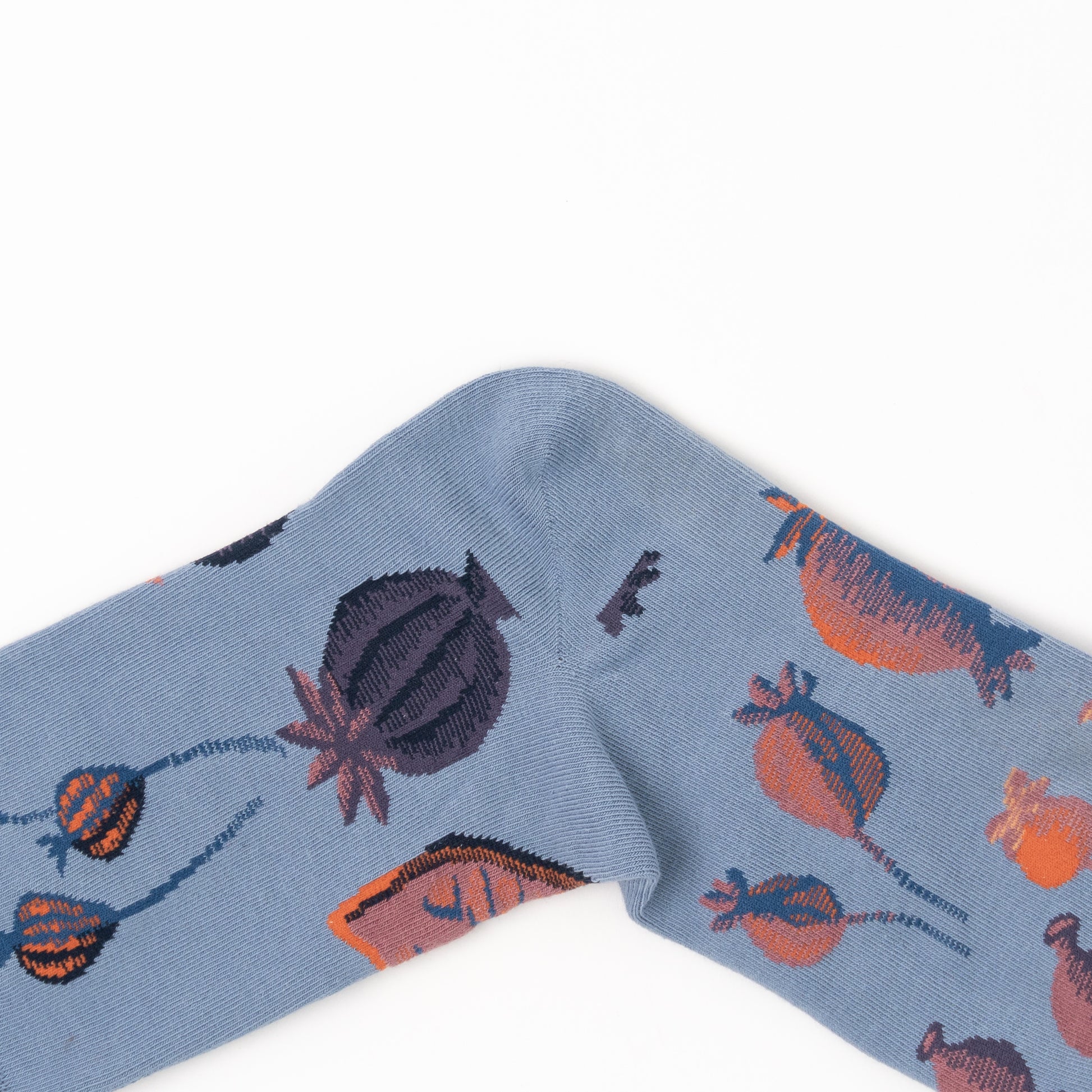 Close-up of a folded sock's heel, showing large orange and plum poppy pod illustrations on dusty blue fabric.