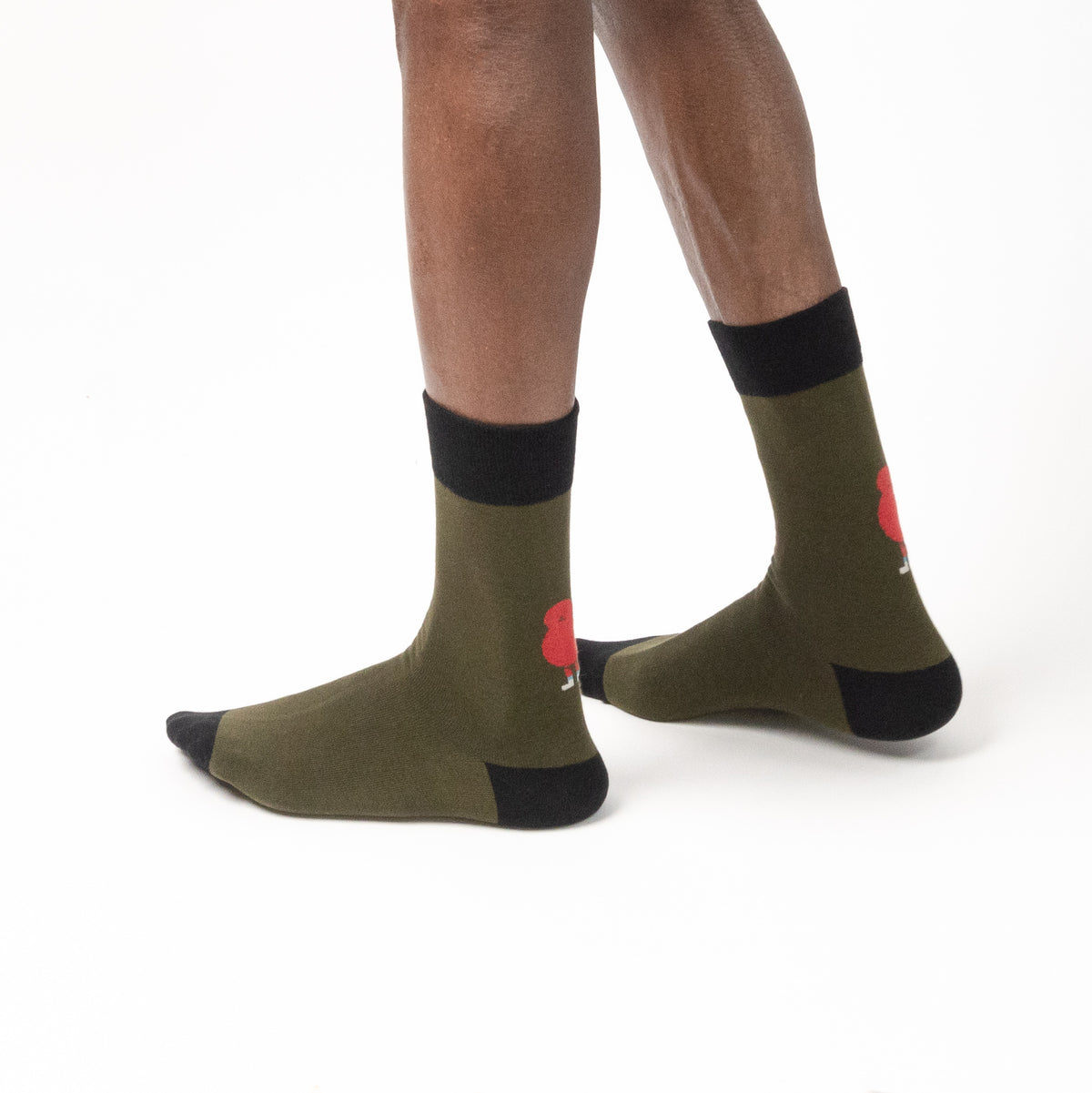 A model wearing olive green crew socks with black toe, heel, and cuff details, featuring a small red rose graphic on the side, against a plain white background.