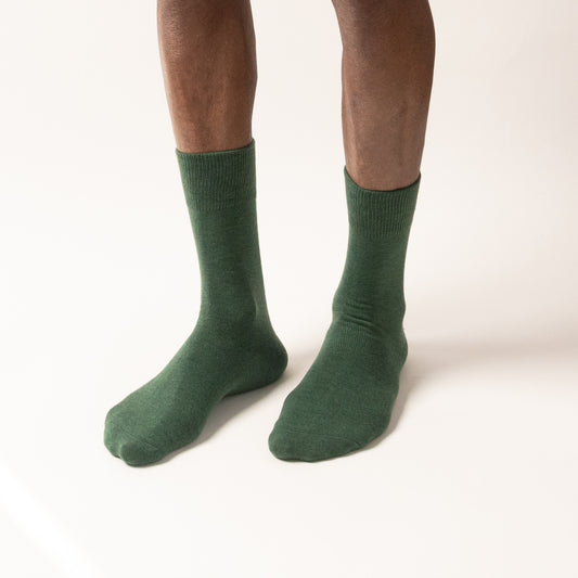 Model standing in solid forest green crew socks with ribbed cuffs, viewed from the front against a white background.