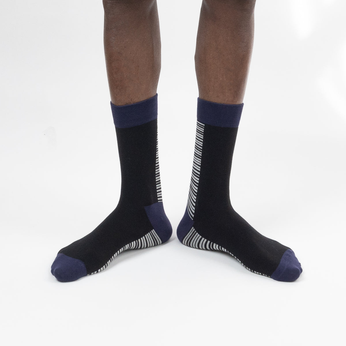 A pair of crew socks worn on a person's feet, shown against a plain white studio background. The socks are primarily black with navy blue cuffs, heels, and toes, and feature white vertical stripe patterns on the sides and soles.