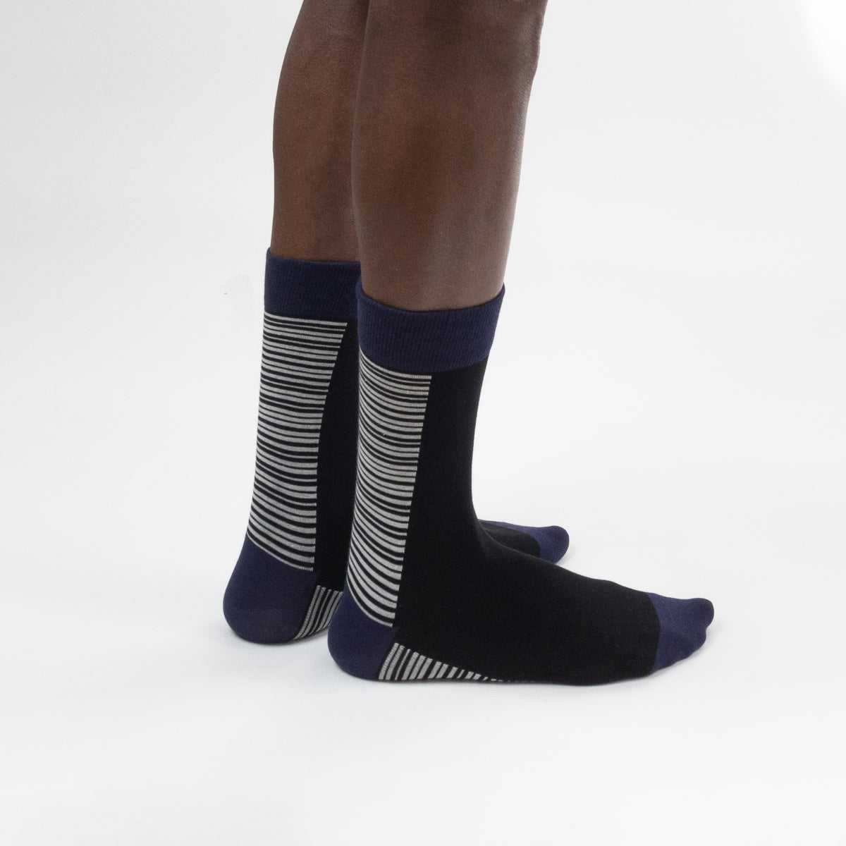 A pair of crew socks worn on a person's feet, shown from the side against a clean white studio background. The socks are primarily black with navy blue cuffs, heels, and toes, and feature gray and white horizontal stripes on the sides.