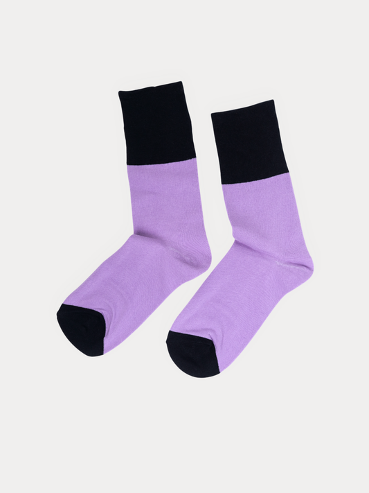 A pair of crew socks laid flat on a light gray background, lavender purple with black cuffs, heels, and toes.