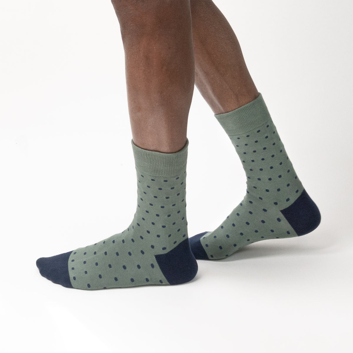 Model wearing sage green patterned socks with navy dots, side view on a white background.