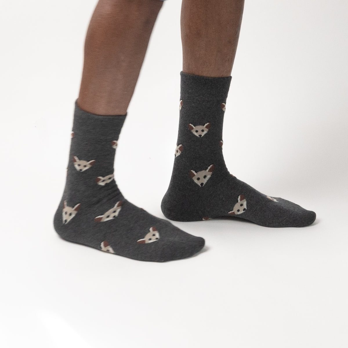 Dark gray crew socks with a repeating pattern of small white and brown fox faces, worn on a person's feet against a plain white studio background.