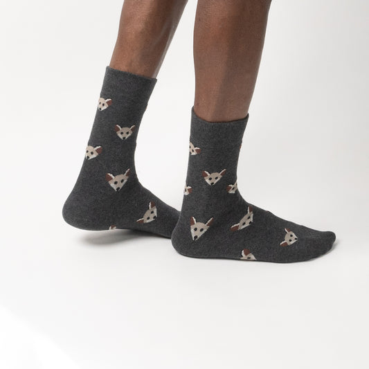 Dark gray crew socks with a repeating pattern of small white and brown fox faces, worn on a person's feet against a clean white studio background.