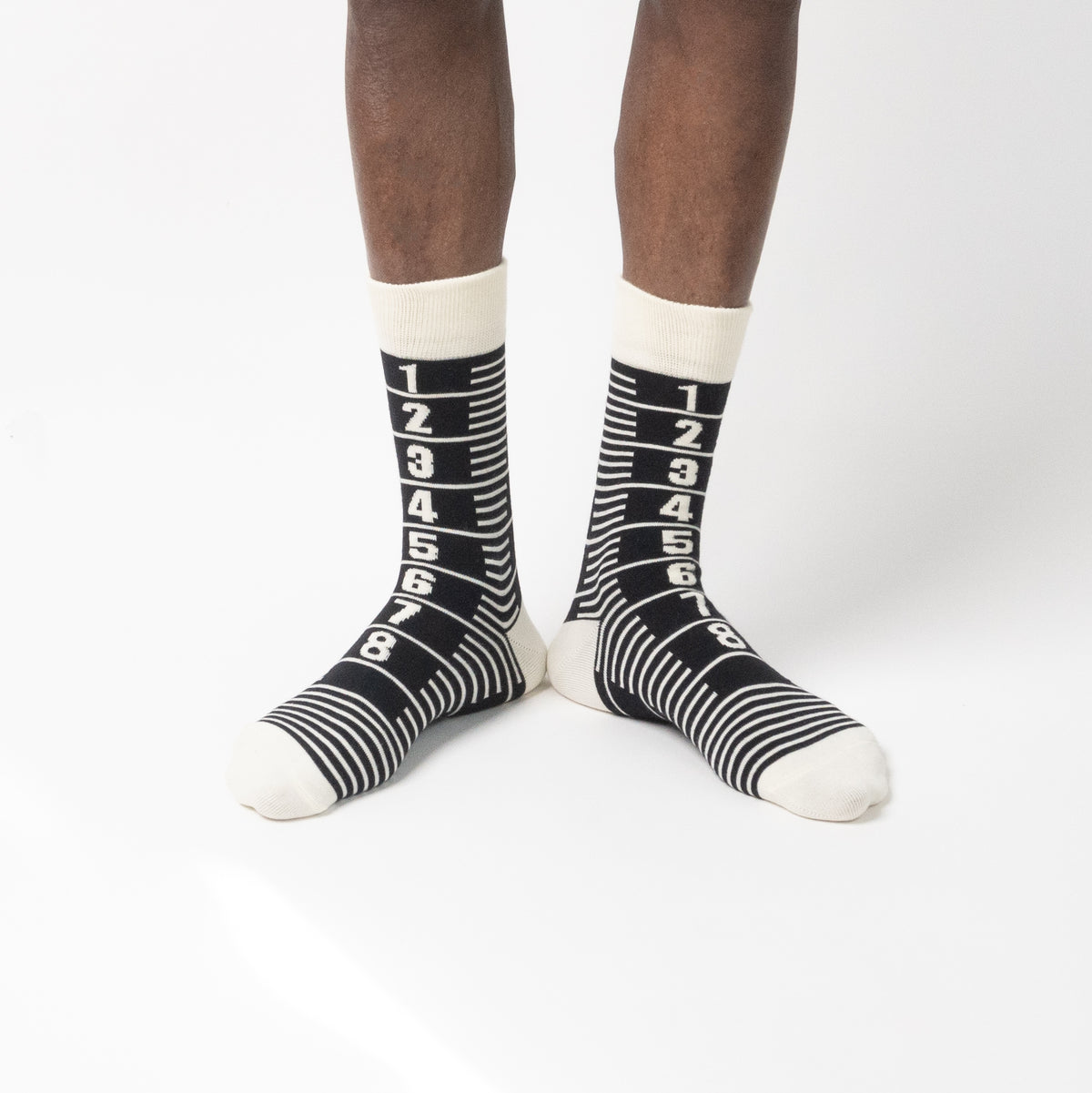 A pair of crew socks with a black and white striped design featuring the number 1 at the top and counting down to 8, worn by a model against a clean white background.