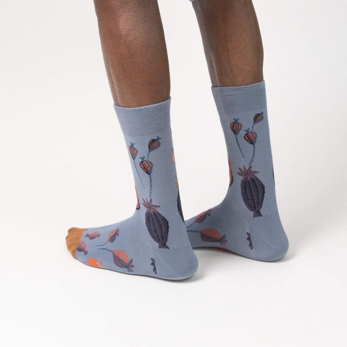 Close-up of slate blue novelty crew socks with a colorful floral and seed pod illustration, isolated on white.