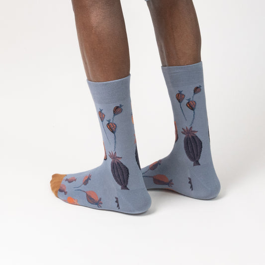Close-up of slate blue novelty crew socks with a colorful floral and seed pod illustration, isolated on white.