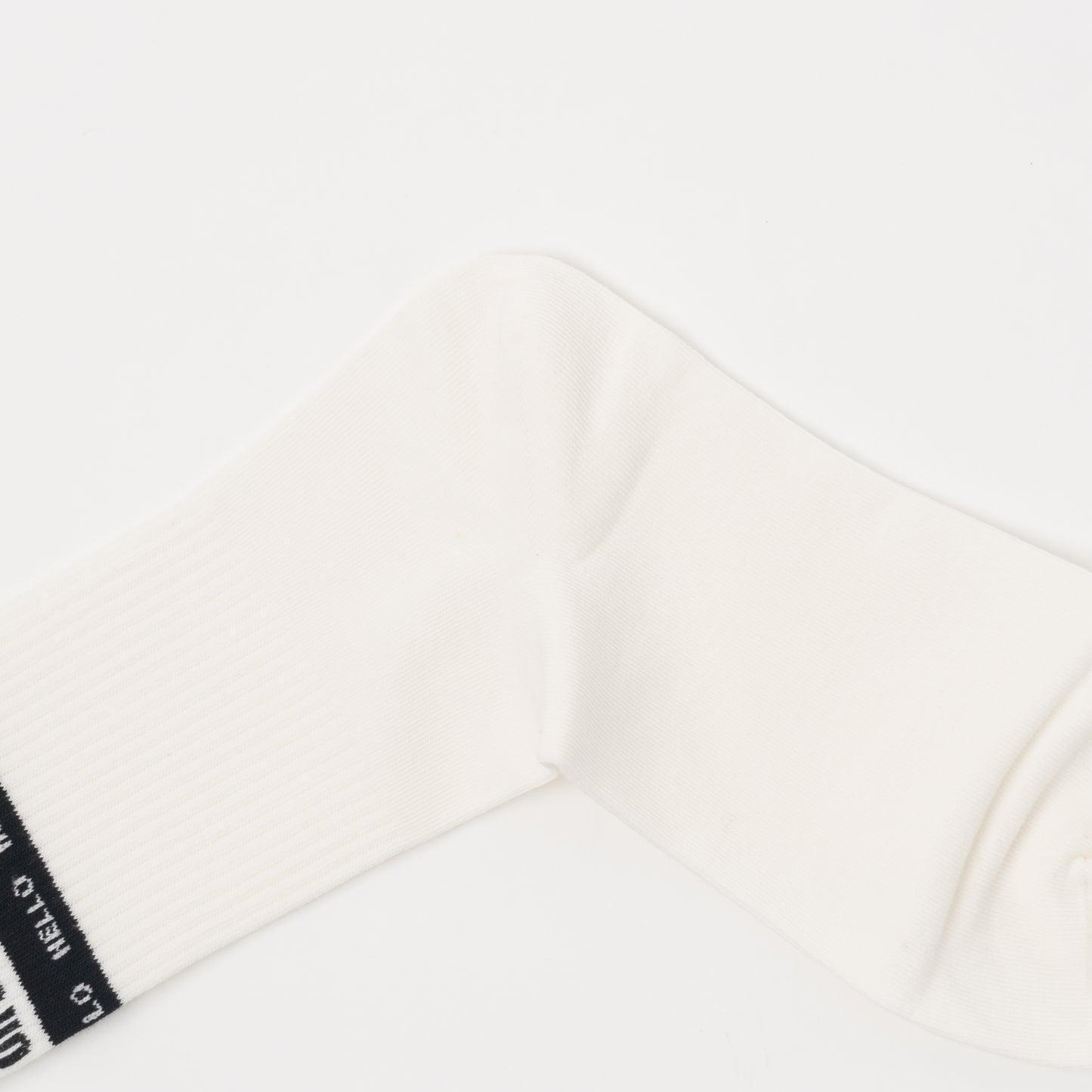 An off-white ribbed sock laid flat on a clean white background, showing a black fabric cuff label with white text.