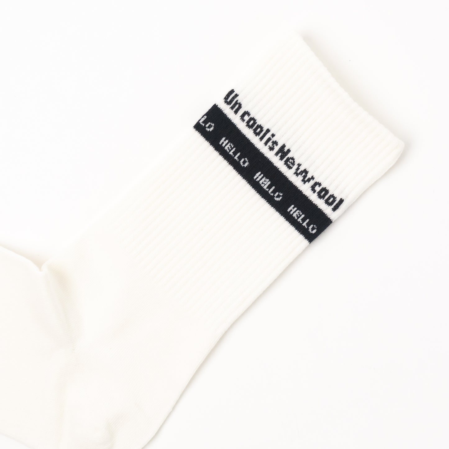 A close-up of a white ribbed sock with a black band near the cuff featuring the text 'Un cool is New cool' and 'HELLO' repeated in white.