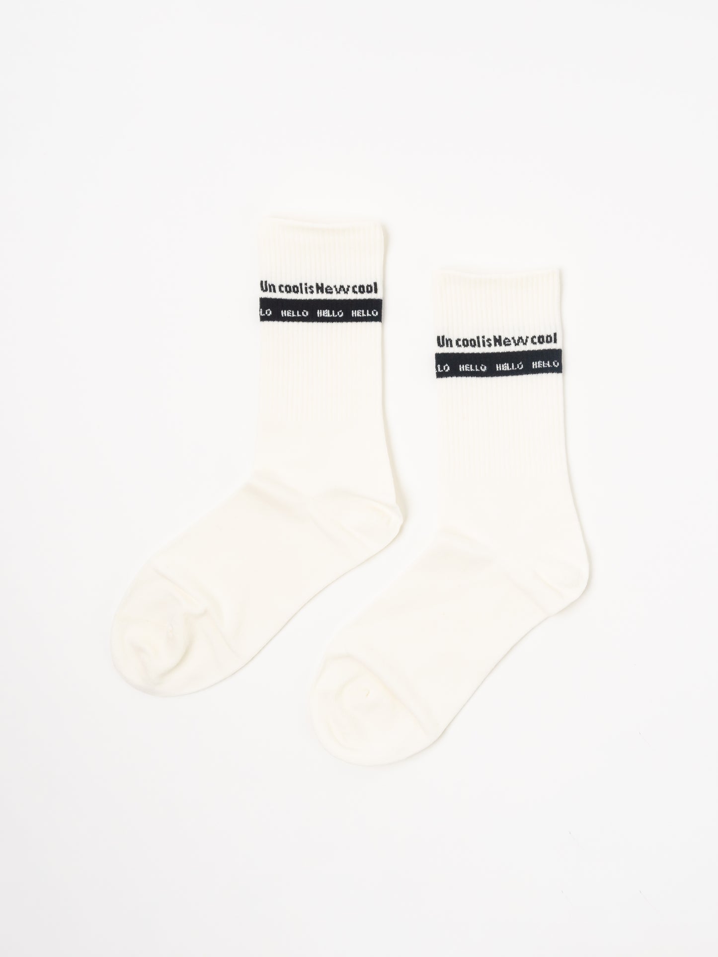 A pair of off-white crew socks with a black band at the top featuring the text 'Uncool is Newcool and 'hello hello', displayed on a clean white background.