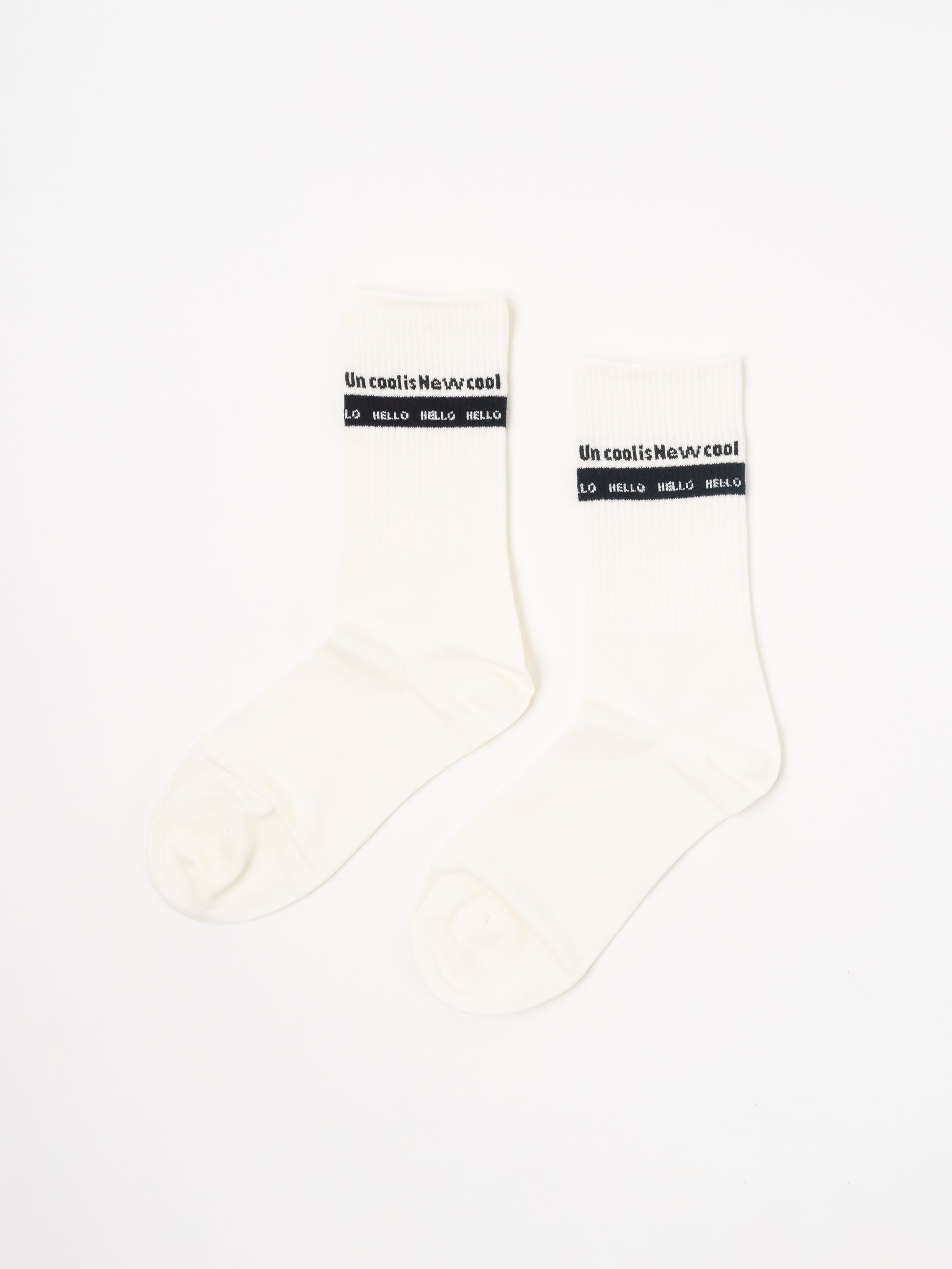 A pair of off-white crew socks with a black band at the top featuring the text 'Uncool is Newcool and 'hello hello', displayed on a clean white background.