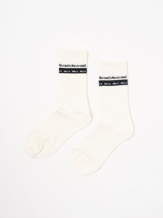 A pair of off-white crew socks with a black band at the top featuring the text 'Uncool is Newcool and 'hello hello', displayed on a clean white background.